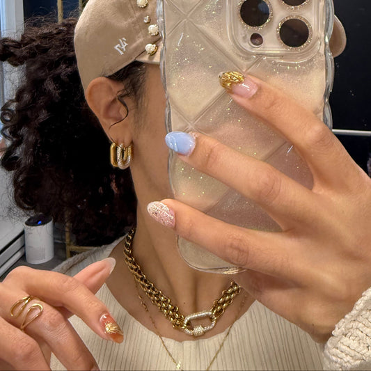 A person showcasing oval hoop earrings in gold color, worn with a cap and accessories.