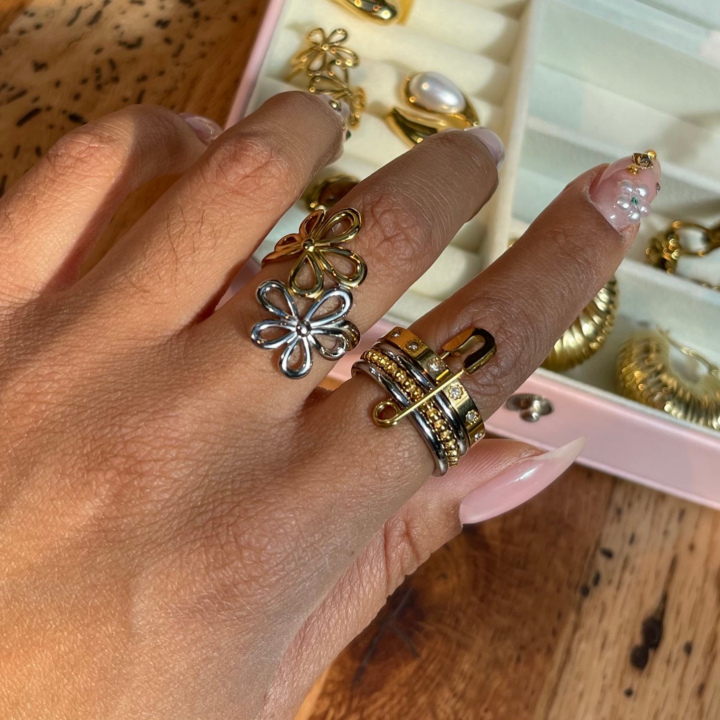Hand wearing multiple gold and silver rings with a jewelry box in the background