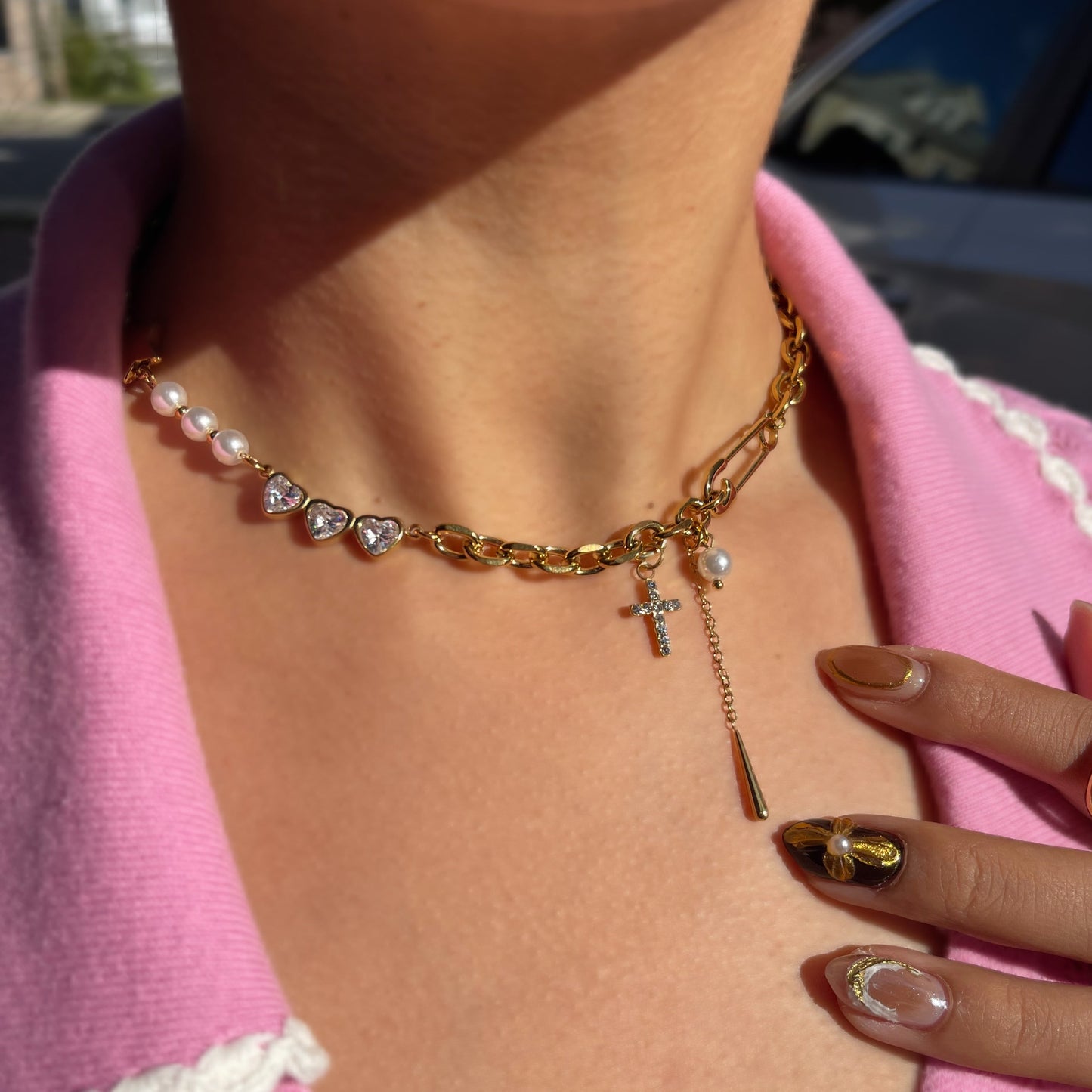 Close-up of a person wearing a gold chain necklace with a cross pendant, set against a blurred outdoor background.