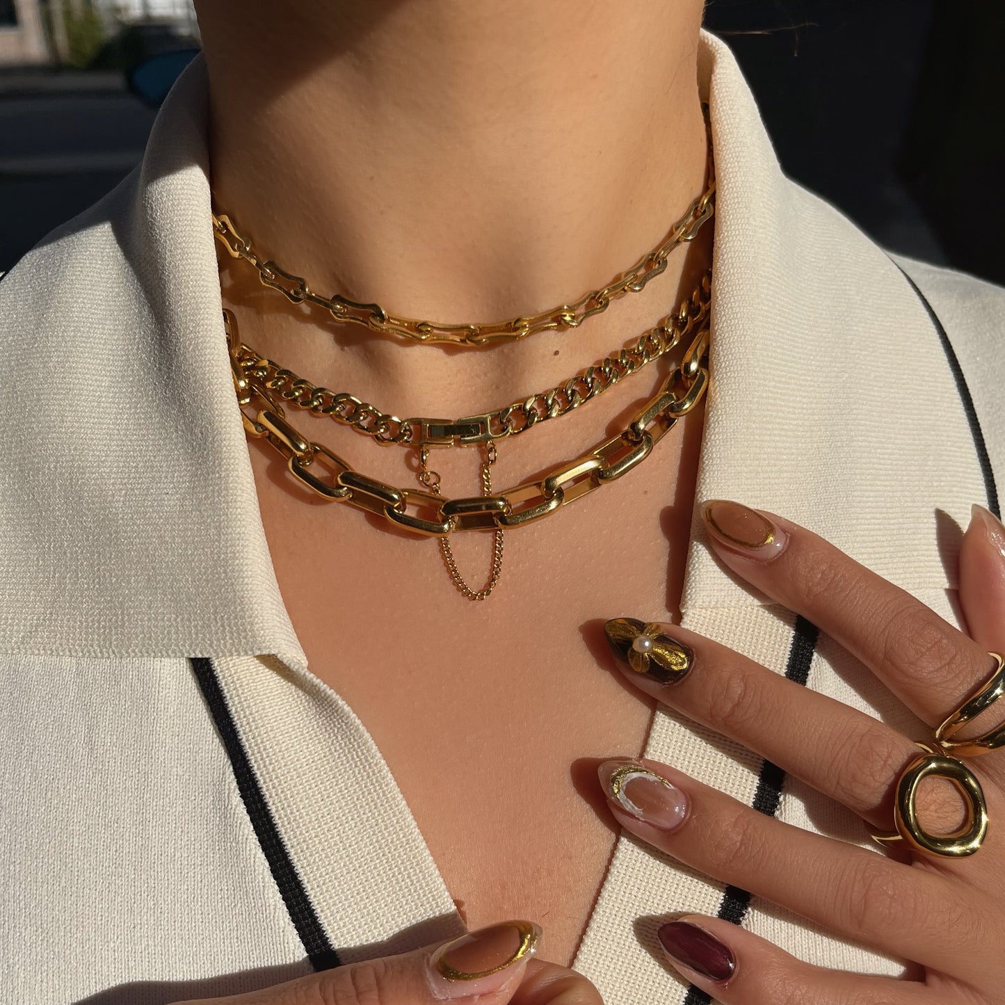 Close-up of gold jewelry including waterproof necklaces and rings on a person wearing a white blazer.