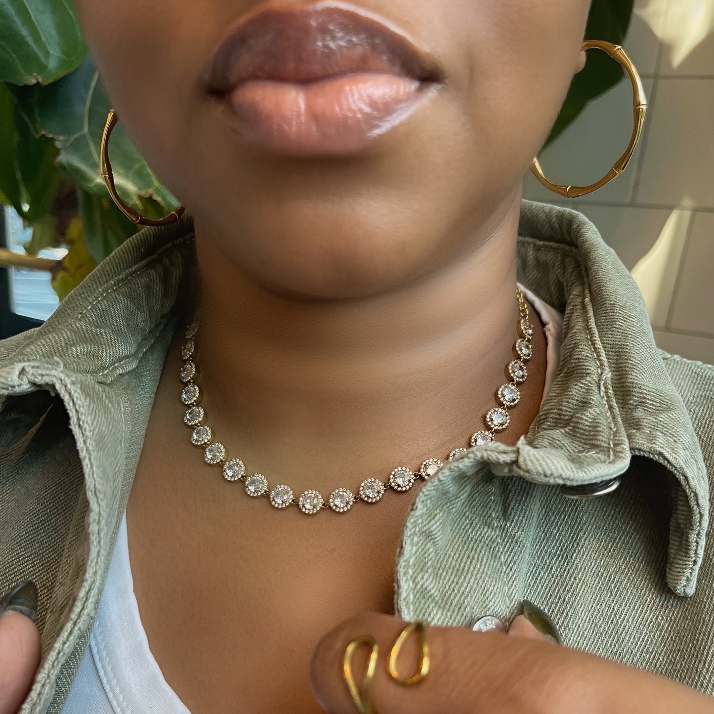 Person wearing a diamond necklace and gold ring with a blurred background