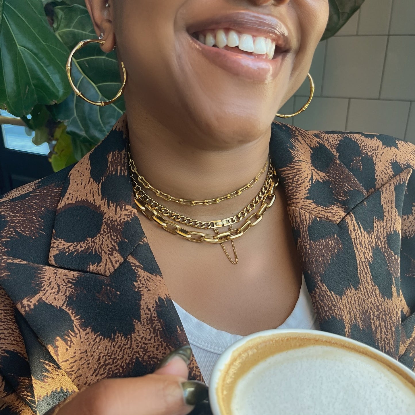 Person holding a cup of coffee with a patterned jacket and gold jewelry.