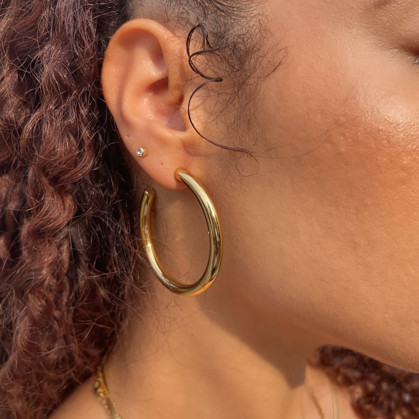 Close-up of a person wearing a 50mm gold hoop earring with a blurred background