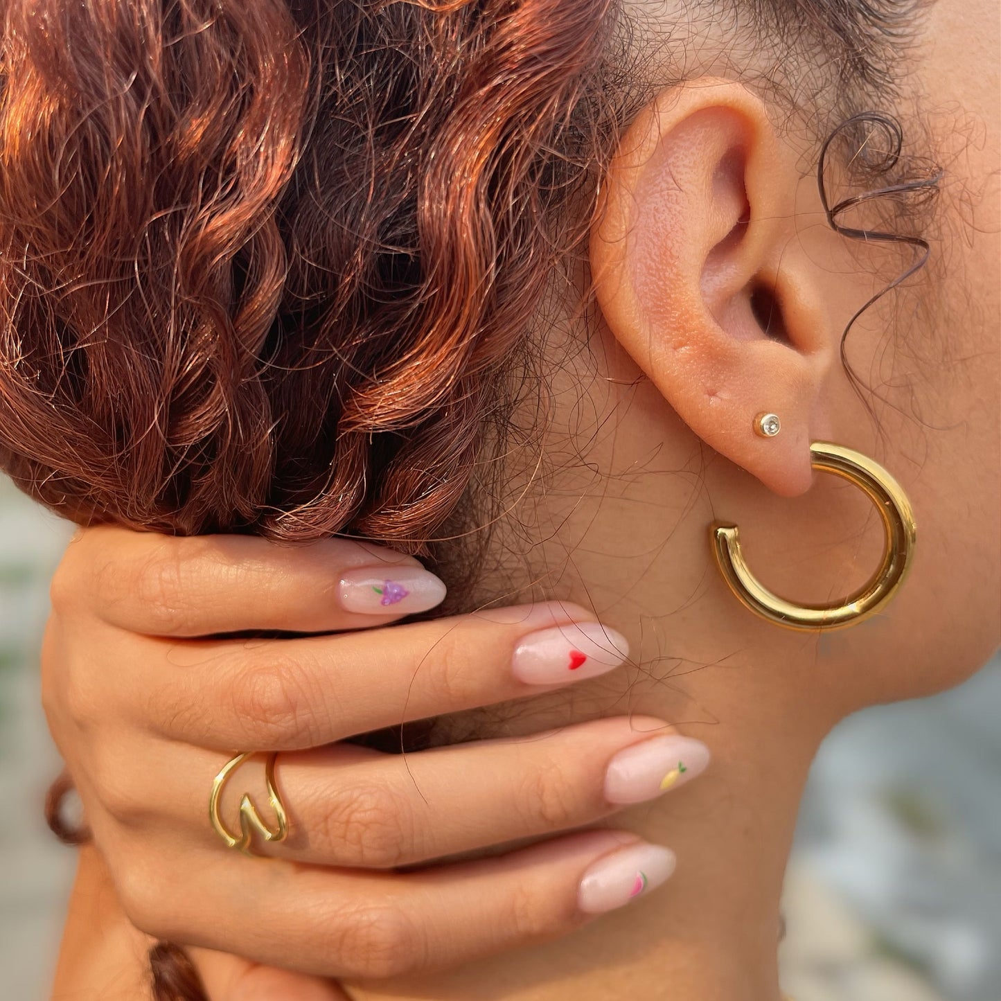 Close-up of a person wearing a 30mm gold hoop earrings and rings with a blurred background