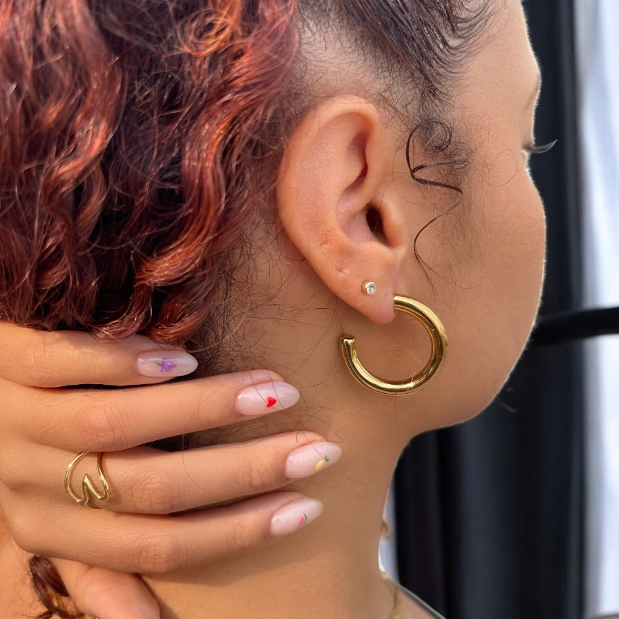 Close-up of a person wearing a 30mm gold hoop earring with a blurred background