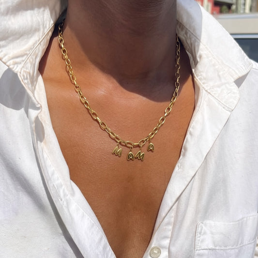 Gold chain necklace with 'MAMA' pendant on a white shirt