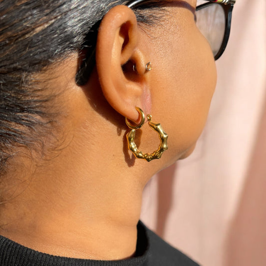 Close-up of an ear wearing a gold bamboo hoop earring with a blurred background