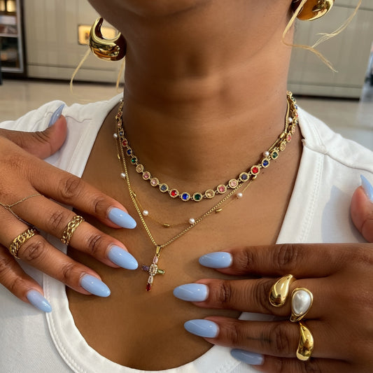 Close-up of a person wearing gold jewelry including necklaces, rings, and earrings with a neutral background.