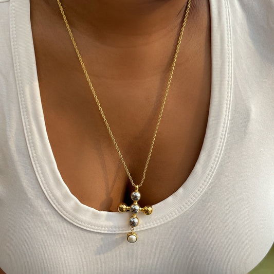 Gold necklace with a cross pendant worn by a person in a white top.