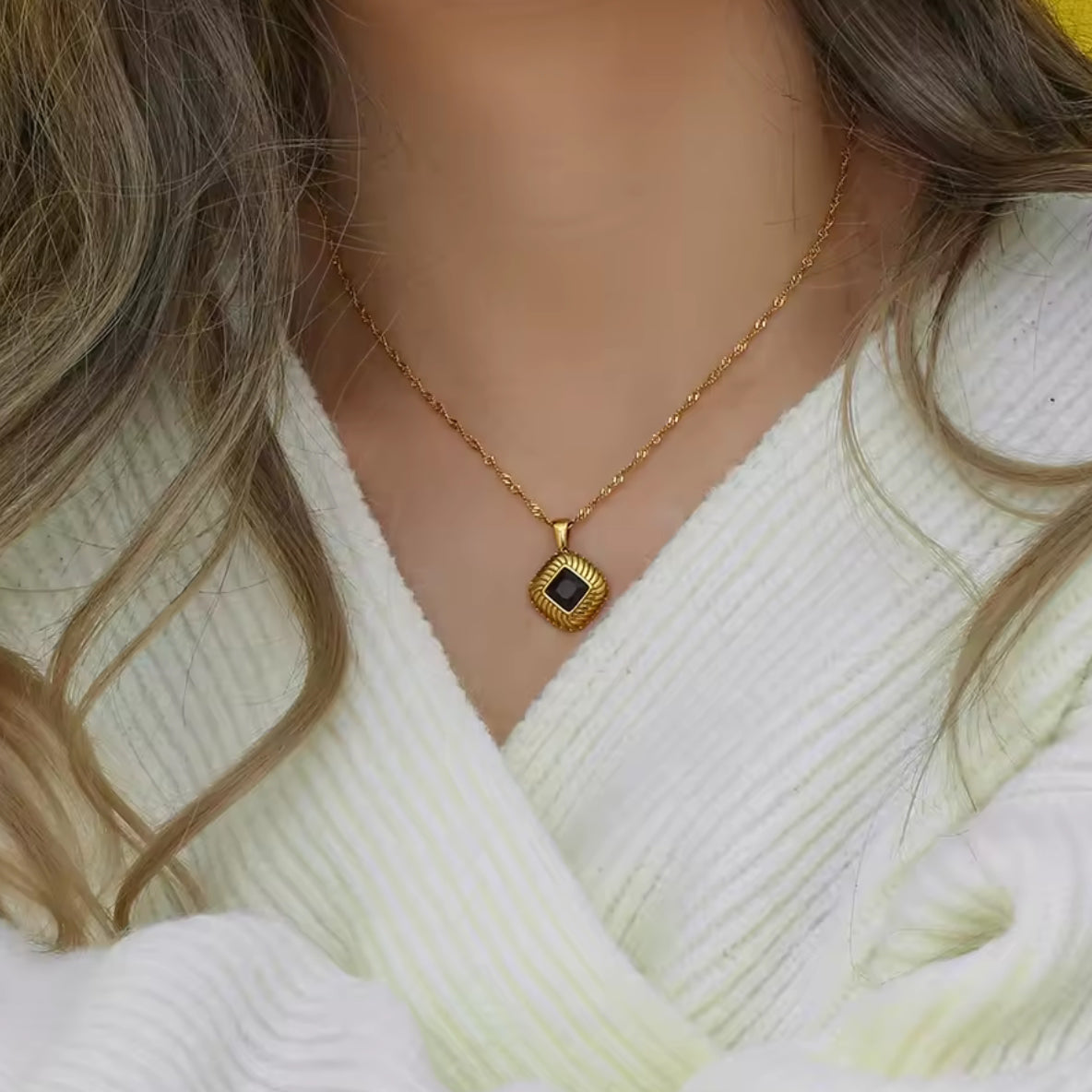 Gold necklace with a black pendant worn by a person in a white sweater.