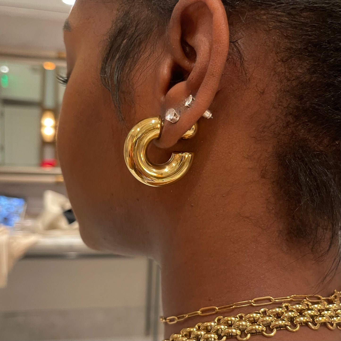 A close-up image of a person's ear wearing a gold chunky C curve hoop earring.