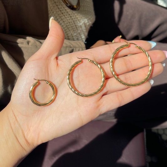 Three gold hoop earrings held in a hand with a blurred background