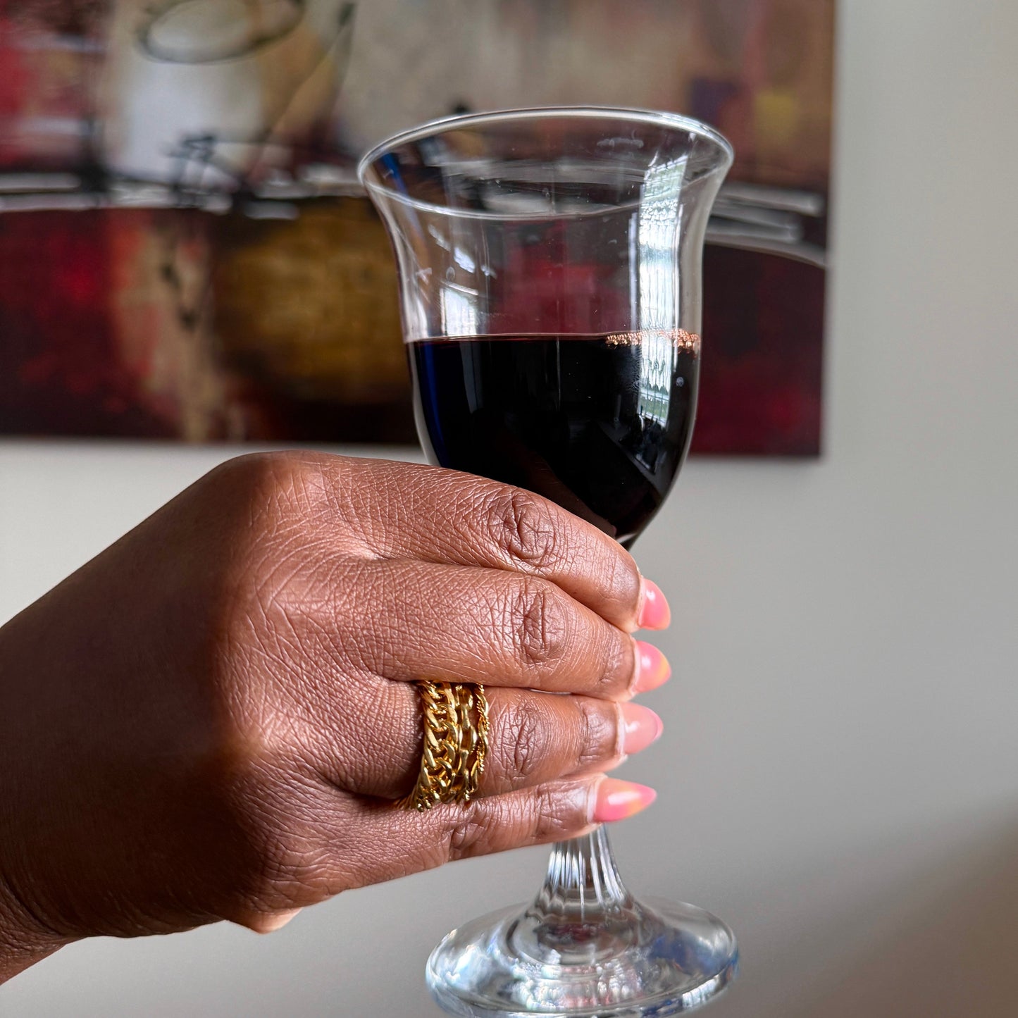 Hand with gold rings holding a glass of red wine with a blurred background