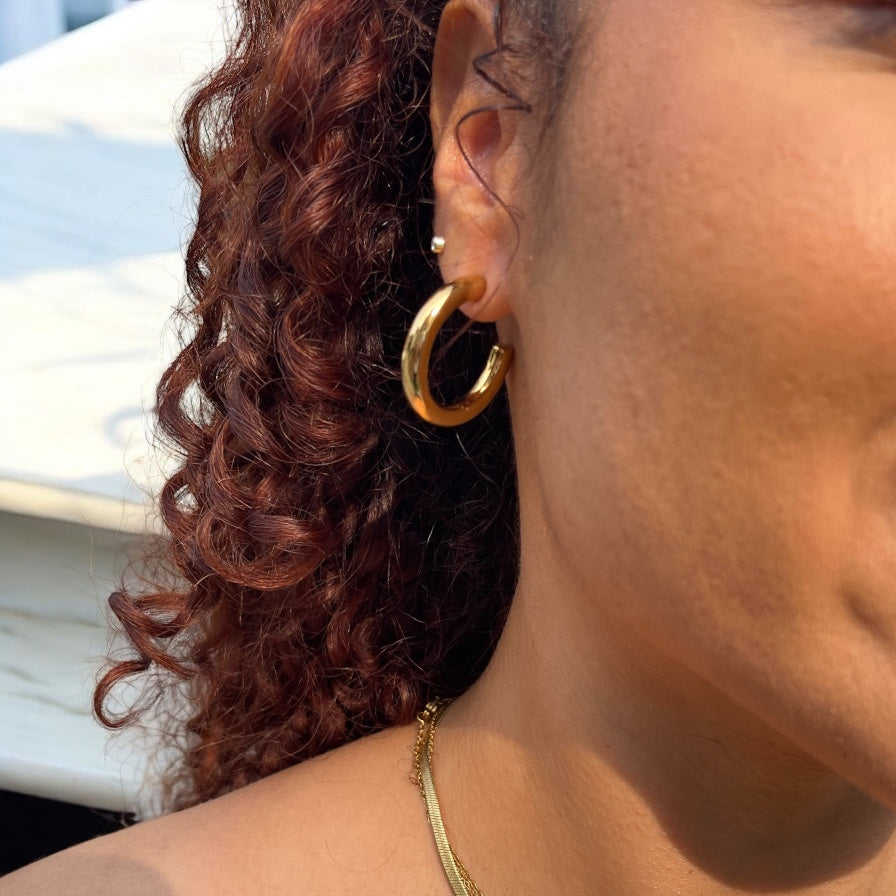 Close-up of a person wearing a 3omm gold hoop earring with blurred background