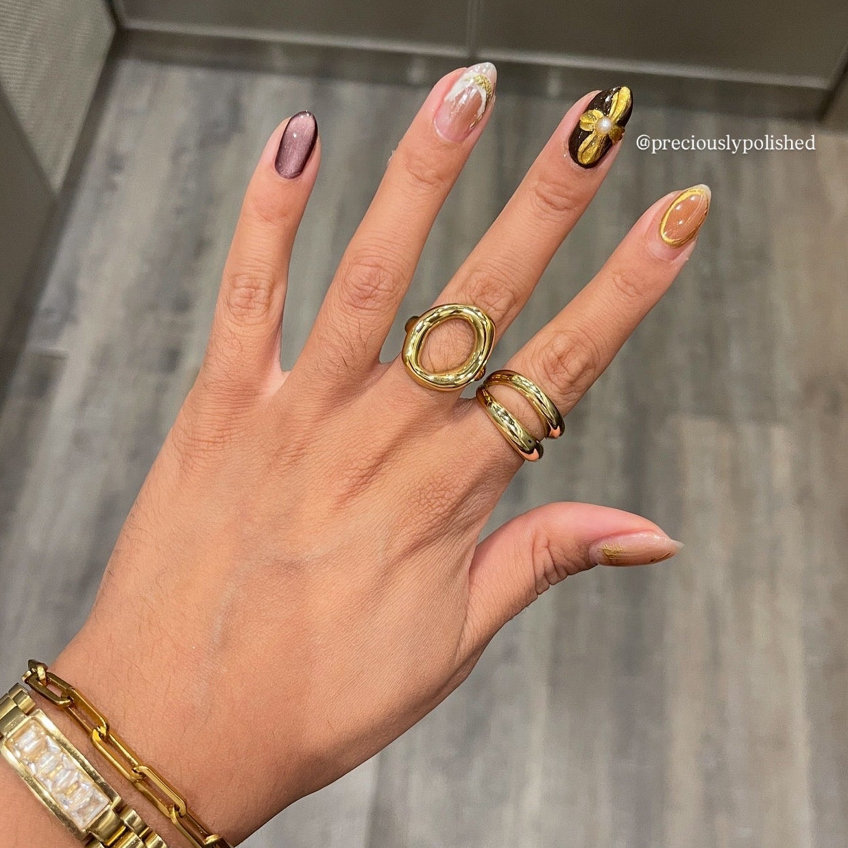 Hand wearing gold rings and bracelet with a neutral background