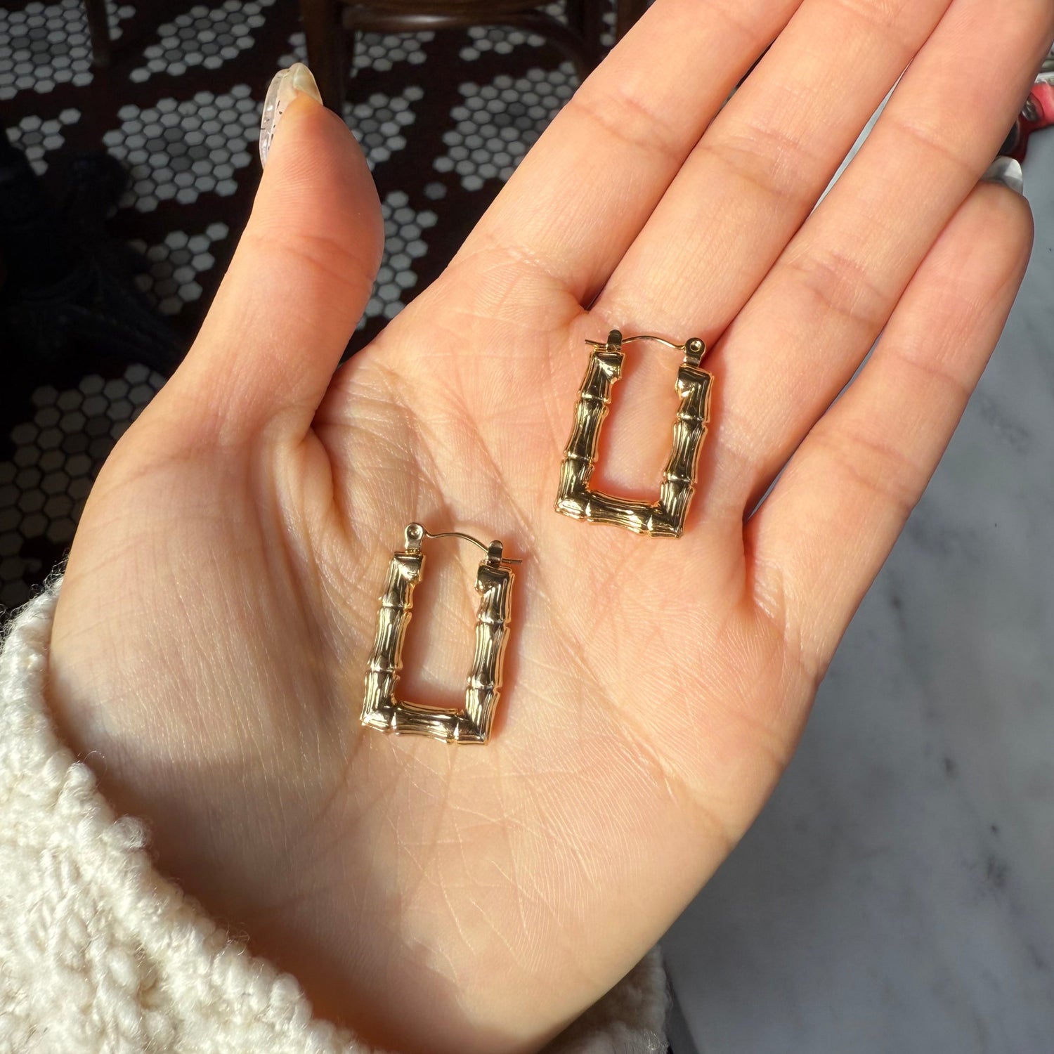 A person's hand holding two small rectangle bamboo earrings with 18k gold plating over stainless steel.