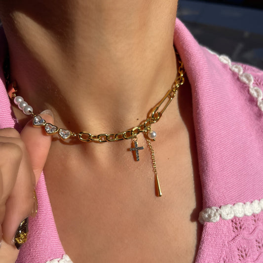 Close-up of a person wearing a gold chain bracelet with a cross charm on a pink outfit.