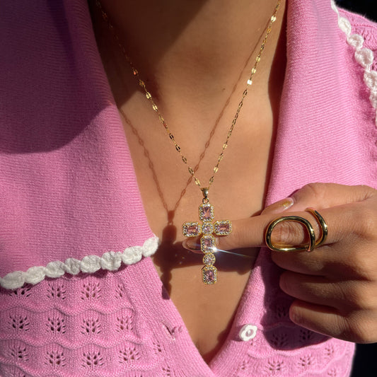 Person wearing a pink textured top with a cross necklace and gold ring.