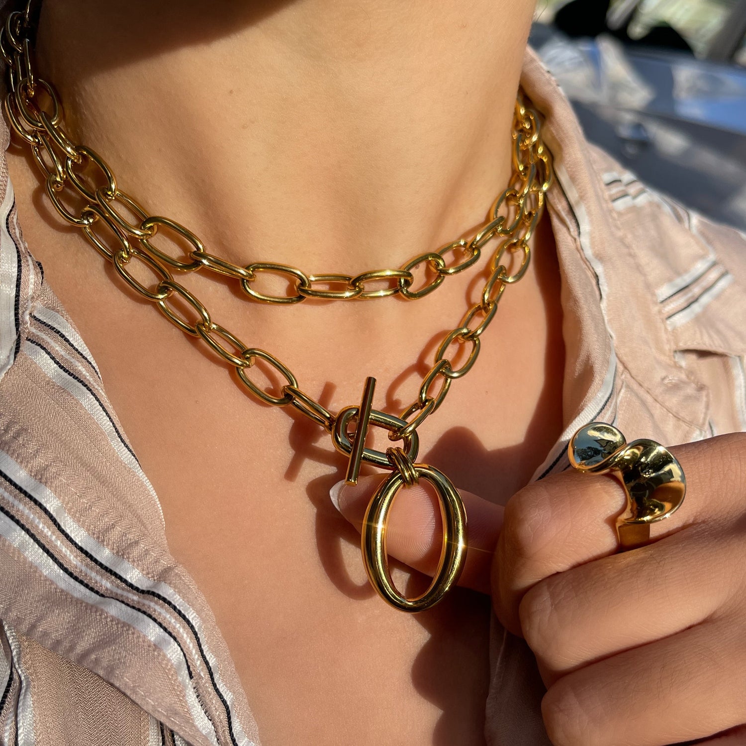 Close-up of a person wearing gold chain necklaces and rings.