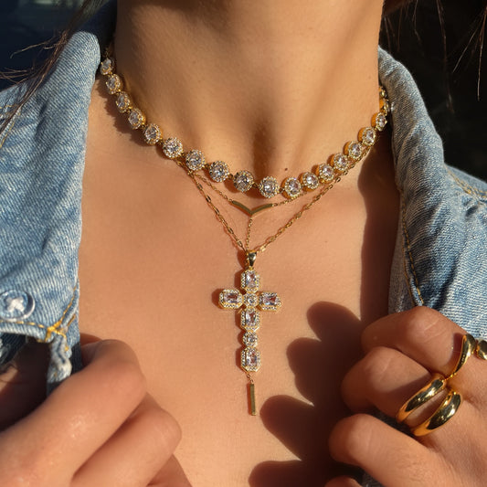 Close-up of a person wearing a gold cross necklace and multiple rings on a denim jacket.