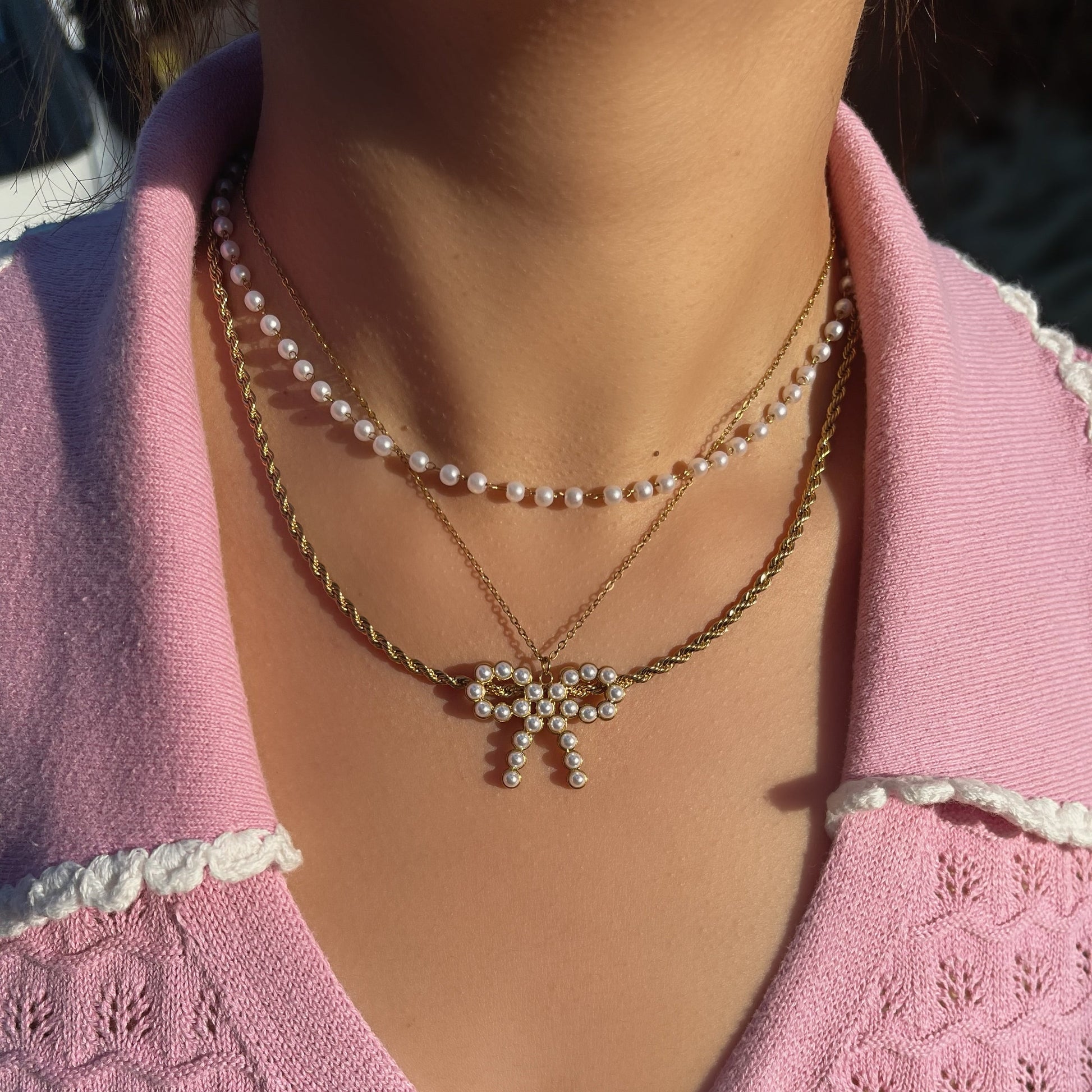 Close-up of a person wearing a pink knitted cardigan with pearl and gold necklaces.
