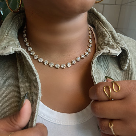 Person wearing a gemstone tennis necklace with gold hoop earrings and rings.
