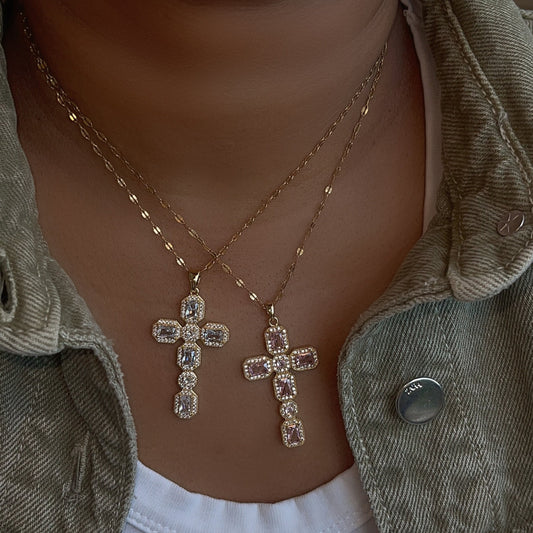 Necklace with a cross pendant worn by a person, with a blurred background.