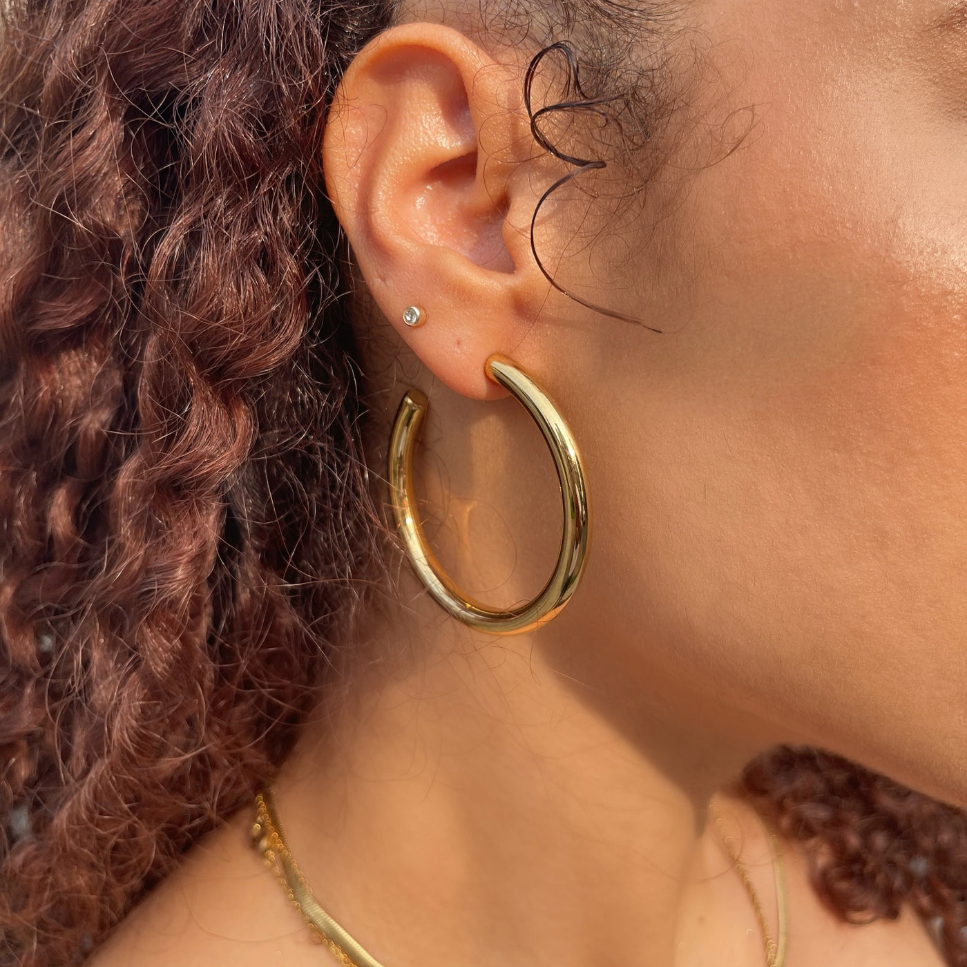 Close-up of a person wearing a 50mm gold hoop earring with another earring visible.