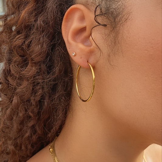 Close-up of a person wearing waterproof gold hoop earrings with a blurred background