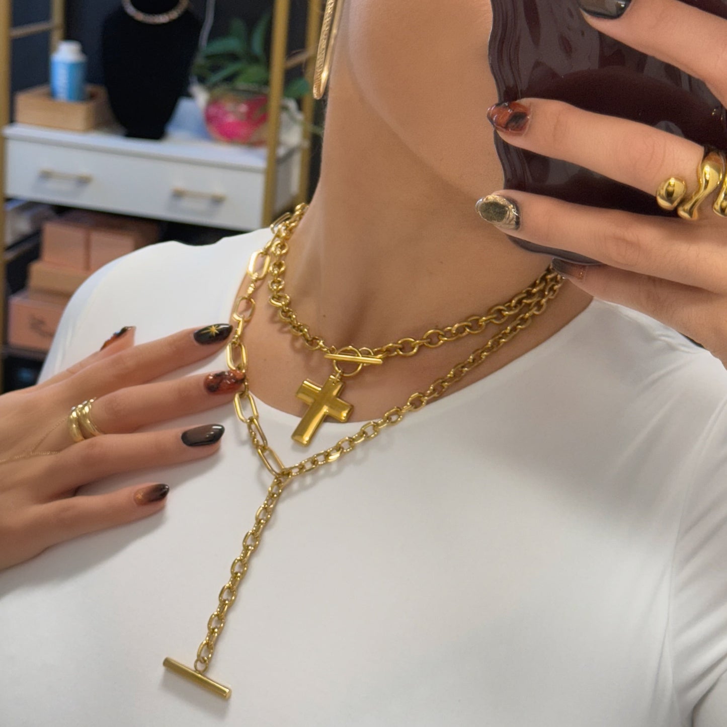 Person wearing a gold necklace with a cross pendant, holding a phone with a dark case.