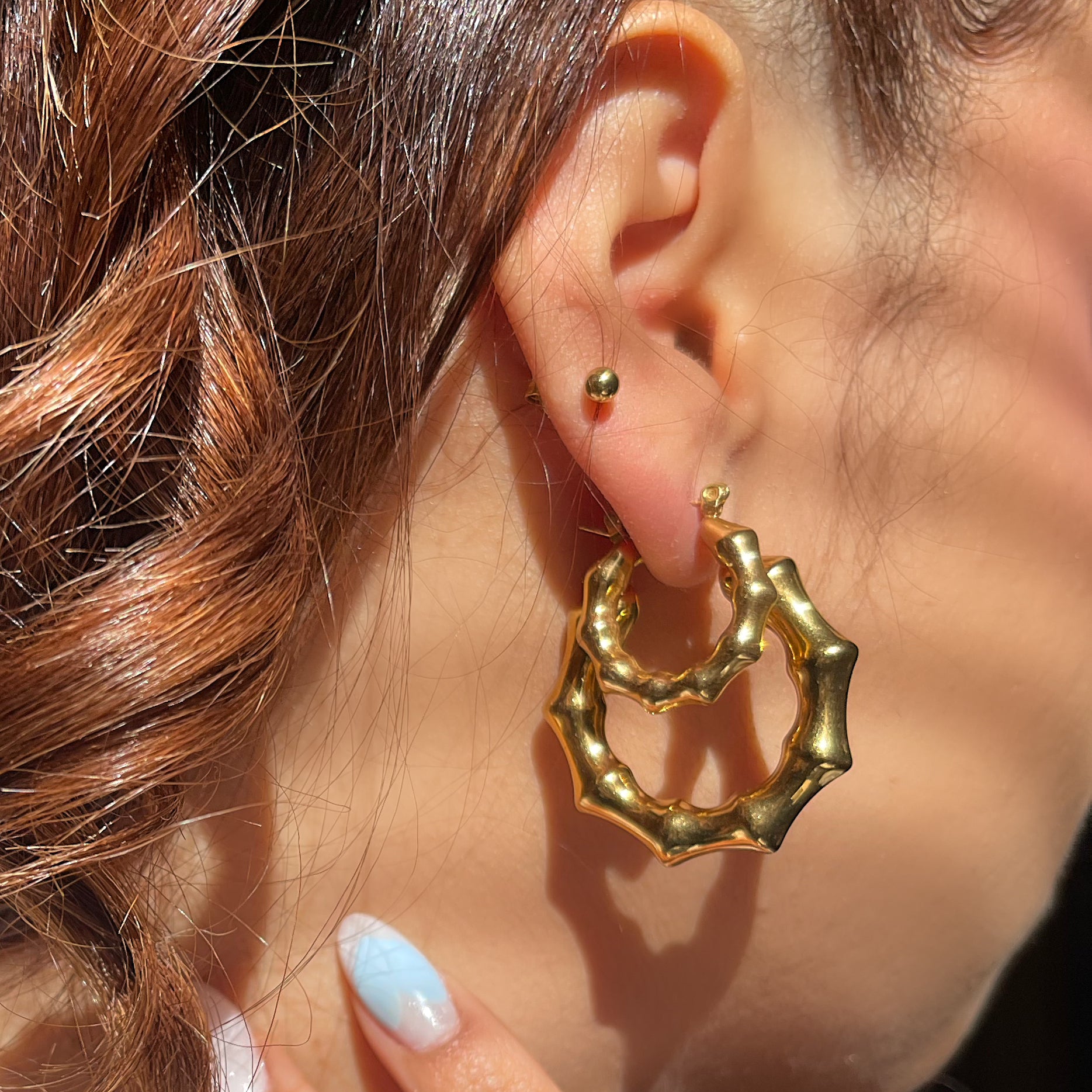 Close-up of a person wearing the Bubble Bamboo Hoop Duo, featuring two gold bamboo-style hoop earrings with a textured, bubbly metallic finish.