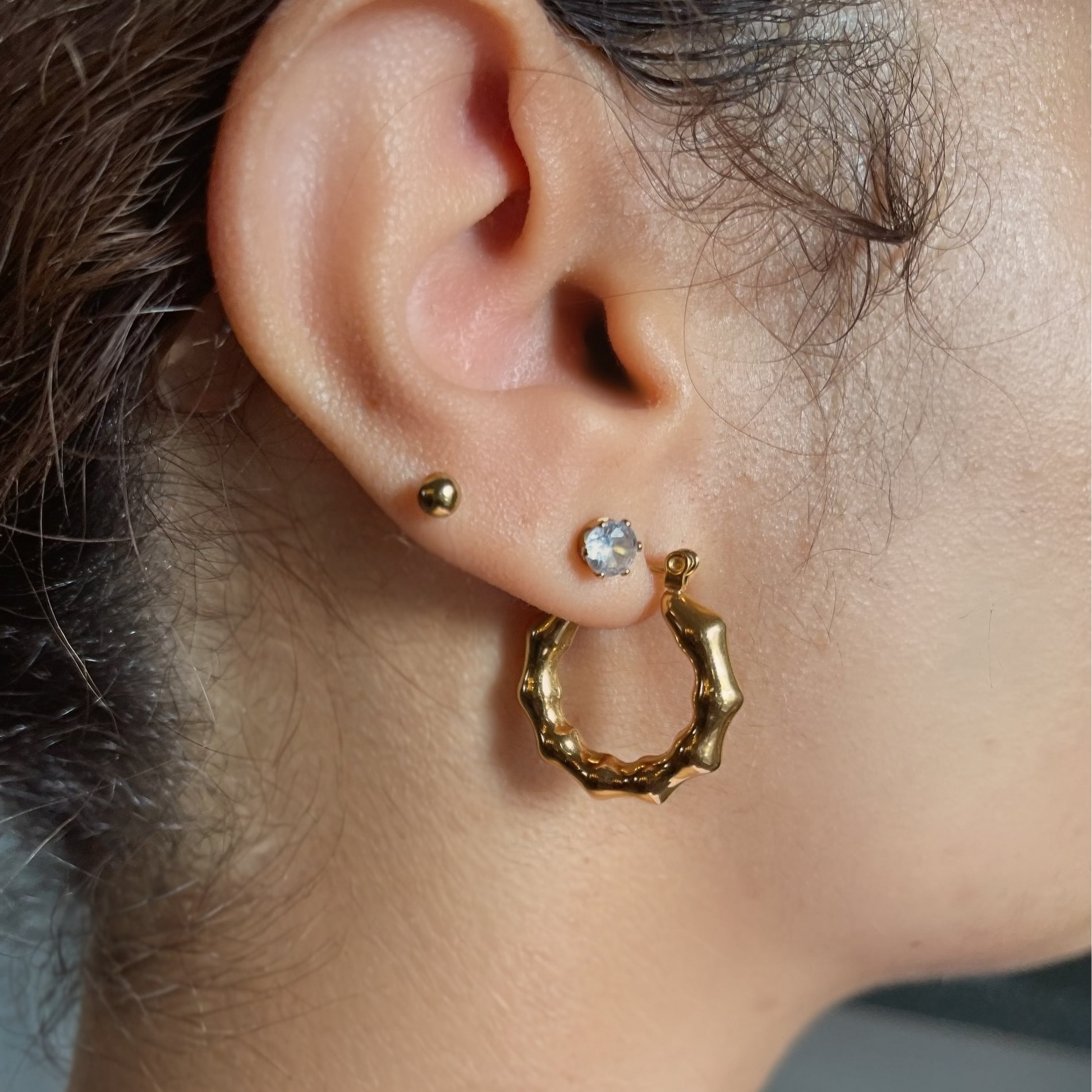 Close-up of an ear wearing gold hoop earrings with a blurred background