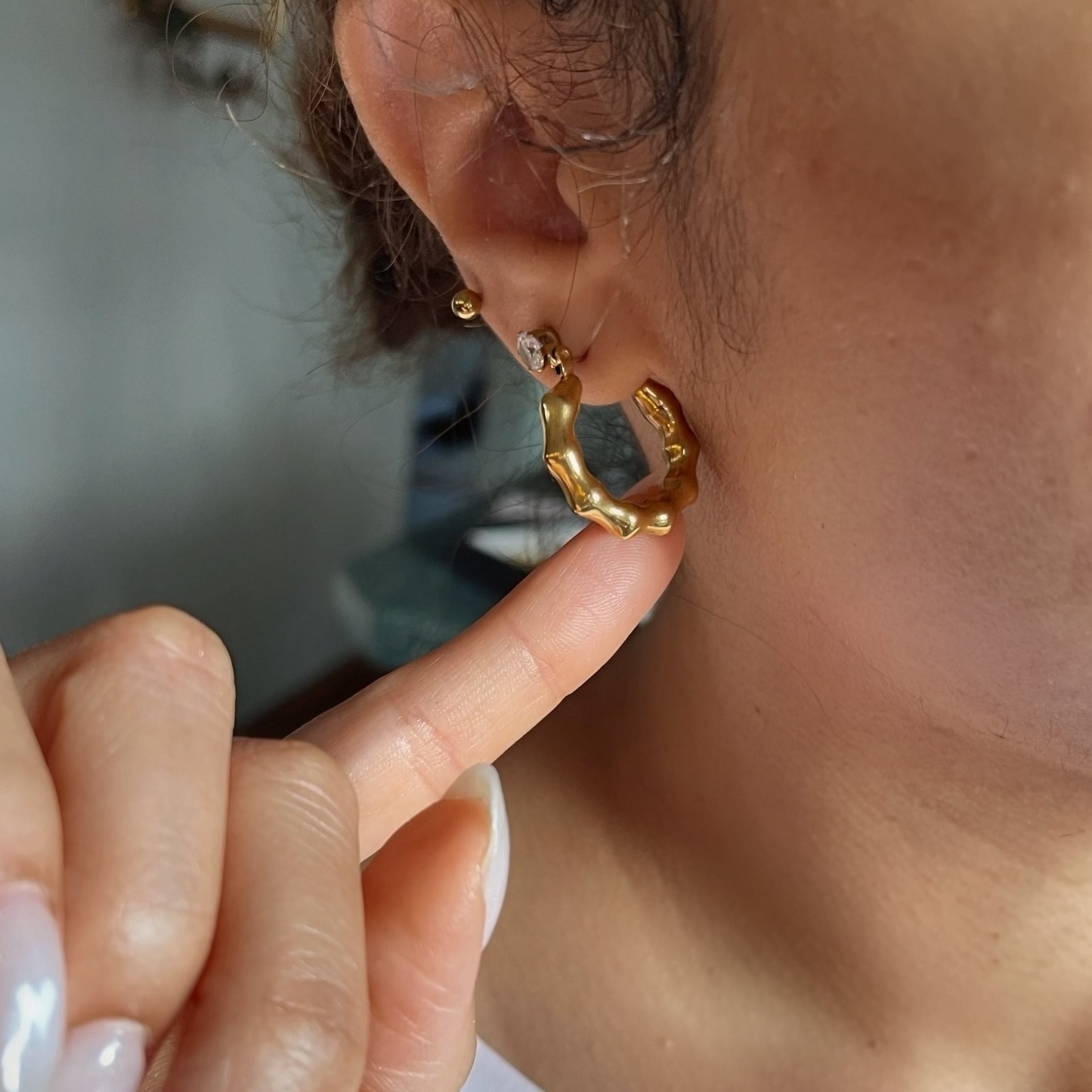 Gold hoop earring being worn and held by a hand with light nail polish.