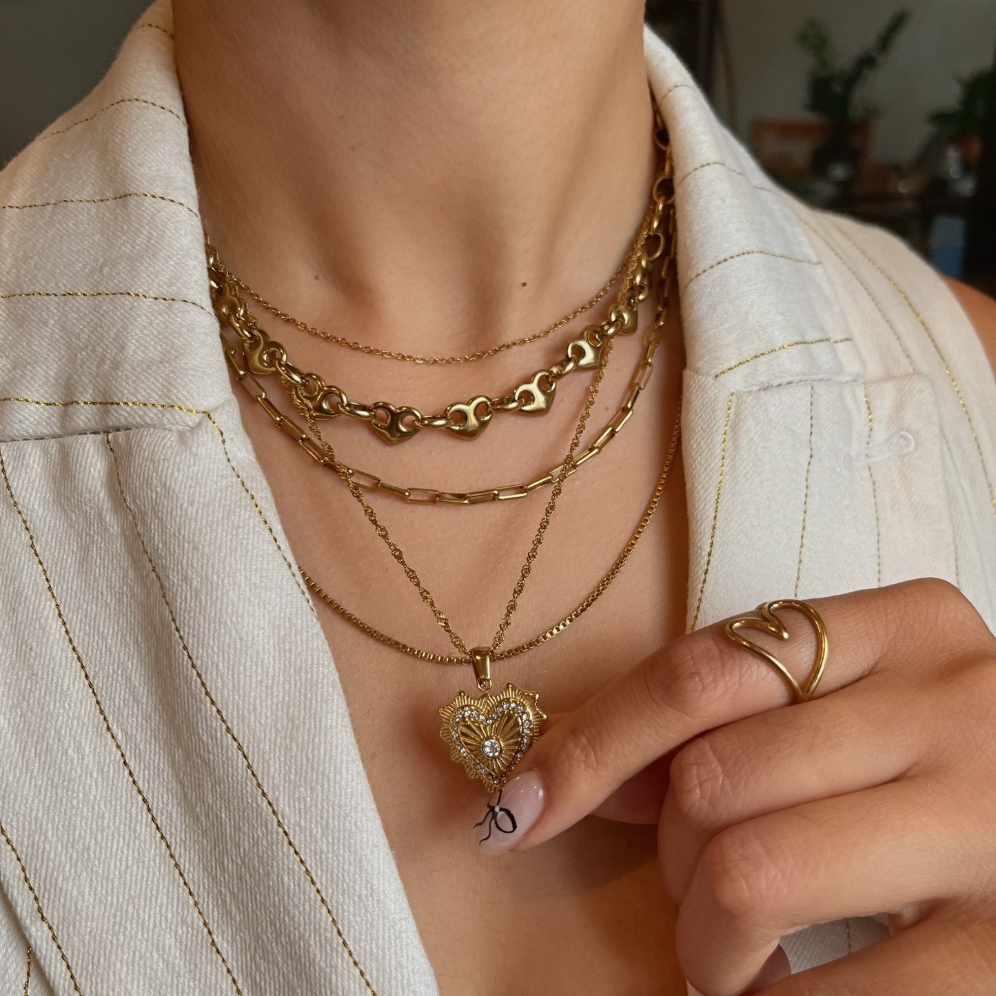 Person wearing multiple gold necklaces with a heart pendant, set against a neutral background.