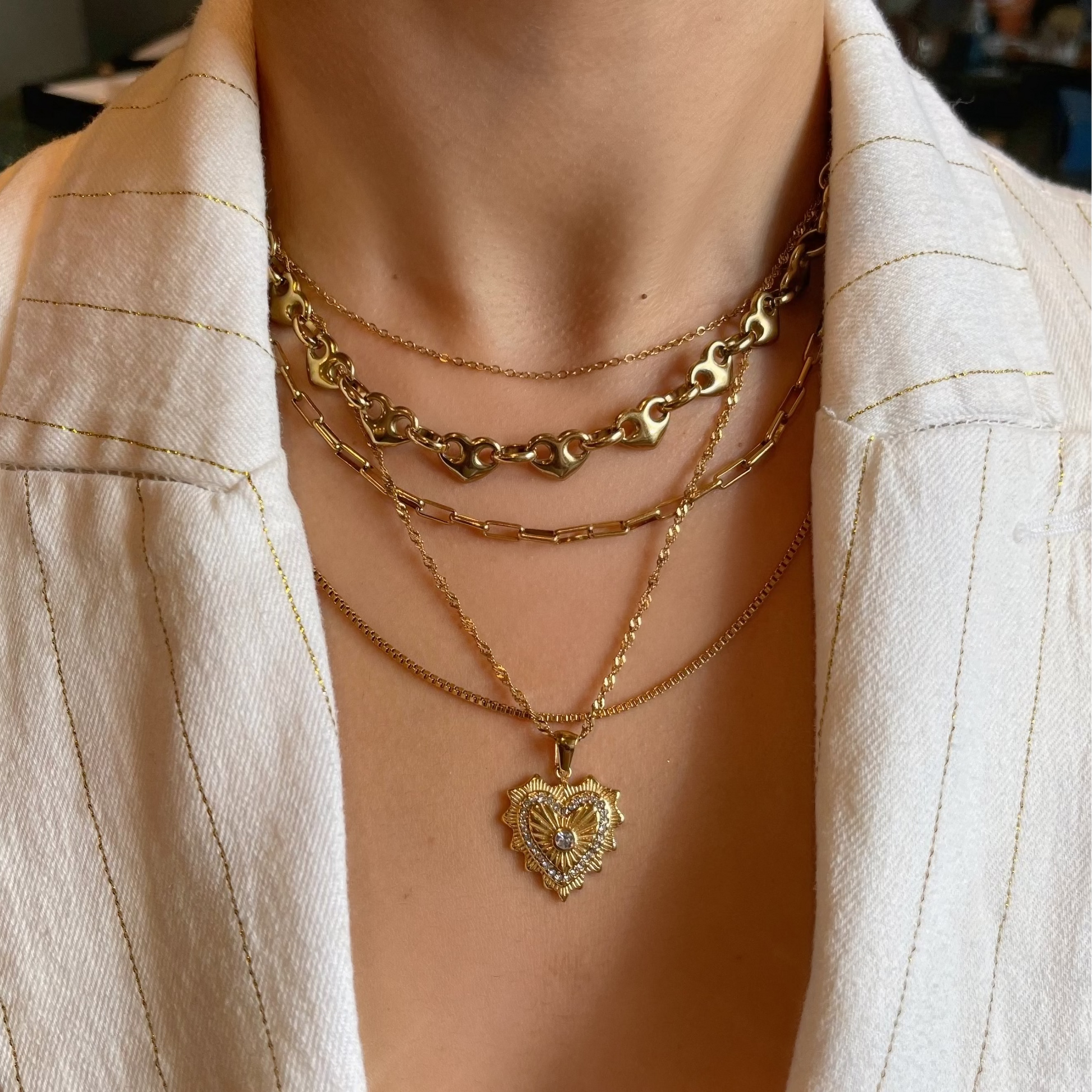 Person wearing multiple gold necklaces with a blurred background