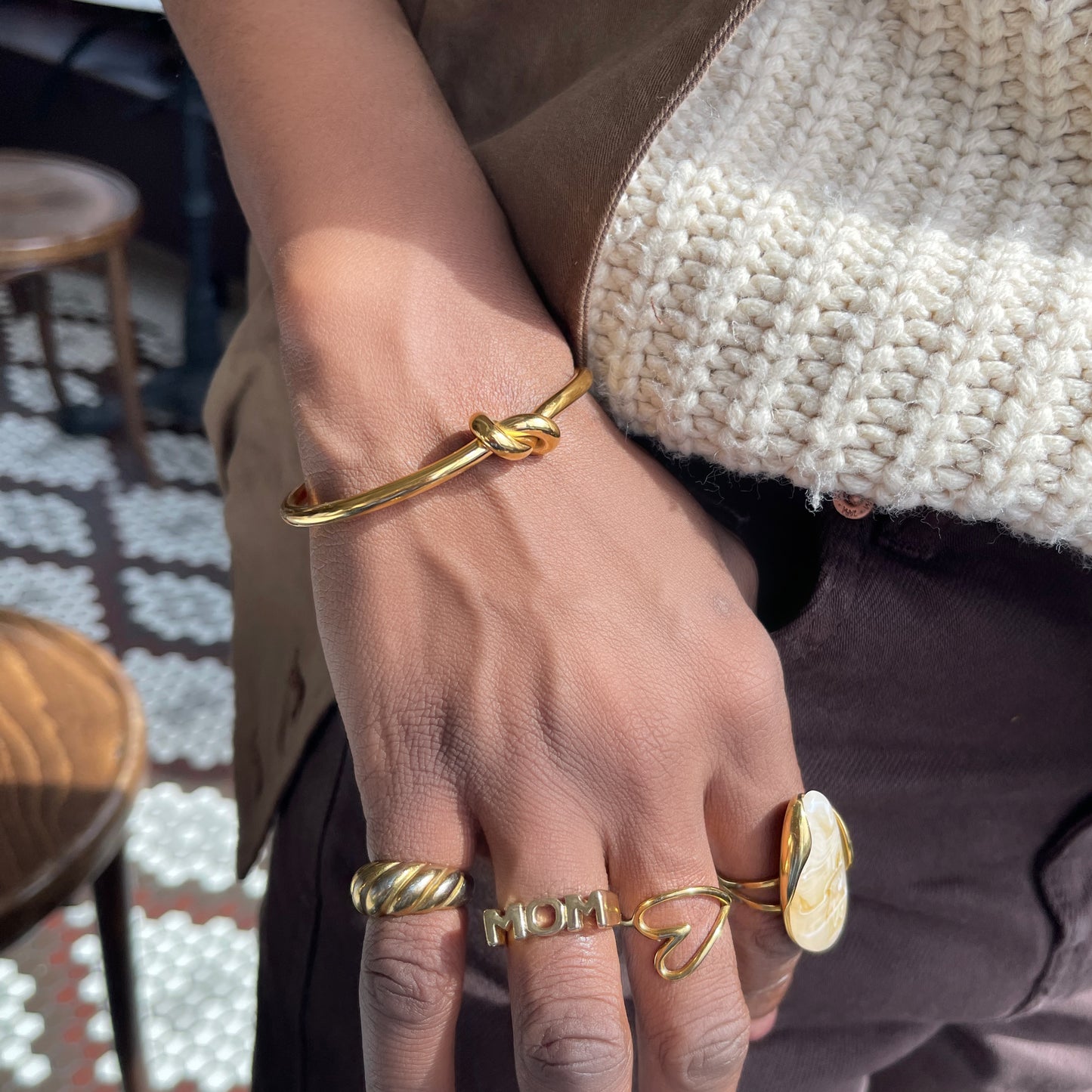 Close-up of a hand wearing multiple gold rings and a bracelet on a blurred indoor background