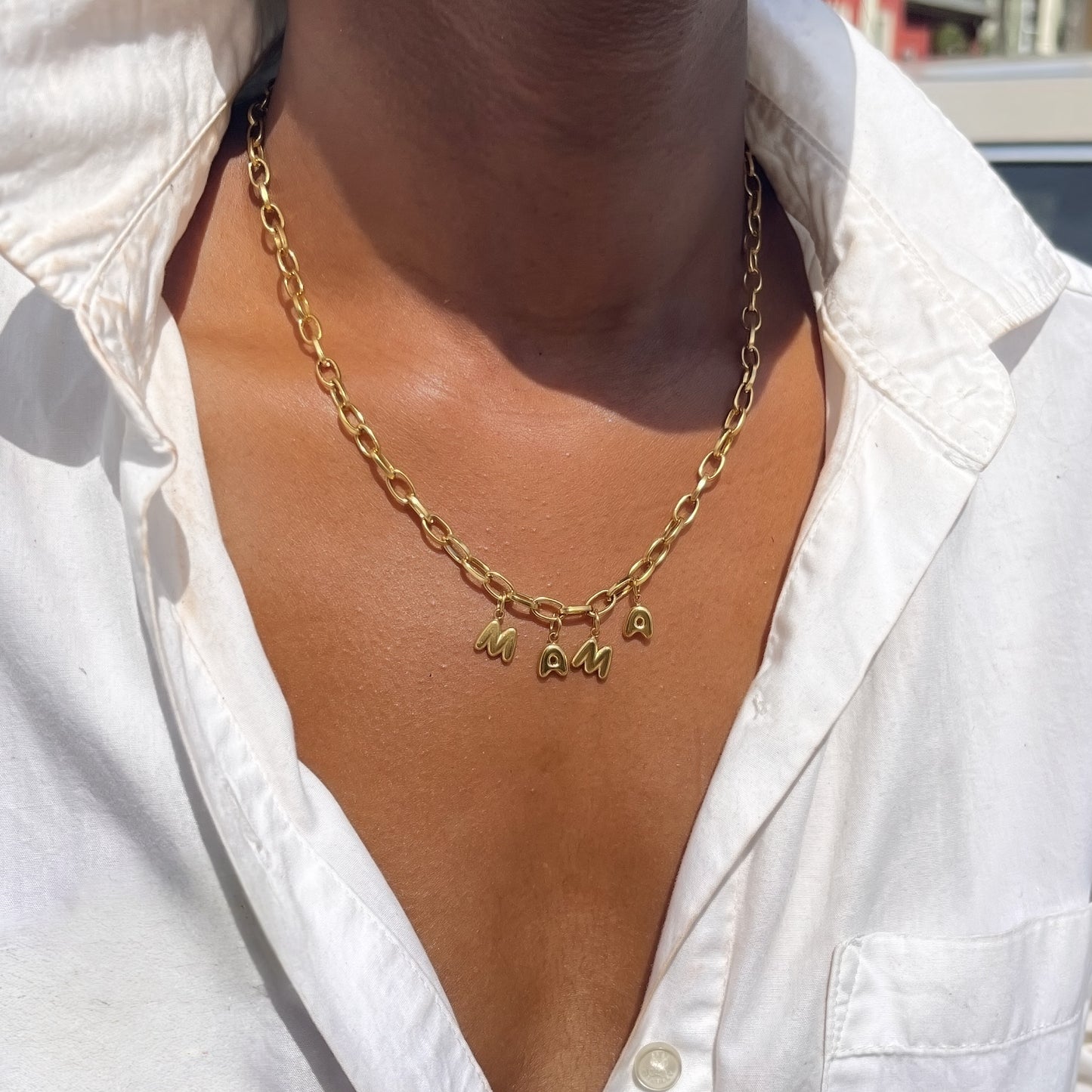 Gold chain necklace with 'MAMA' pendant on a white shirt