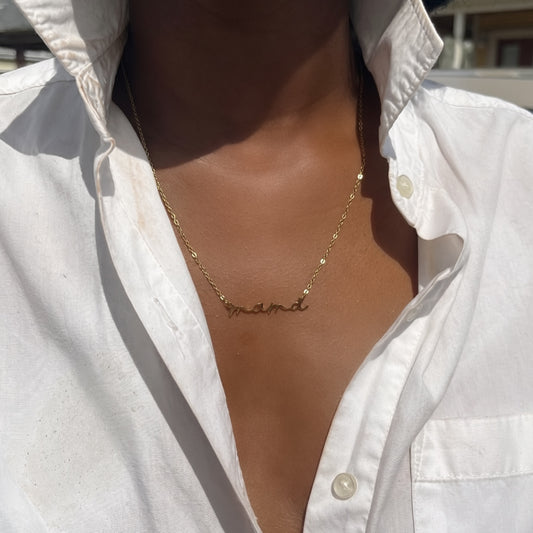 Gold necklace with a name pendant worn by a person in a white shirt.