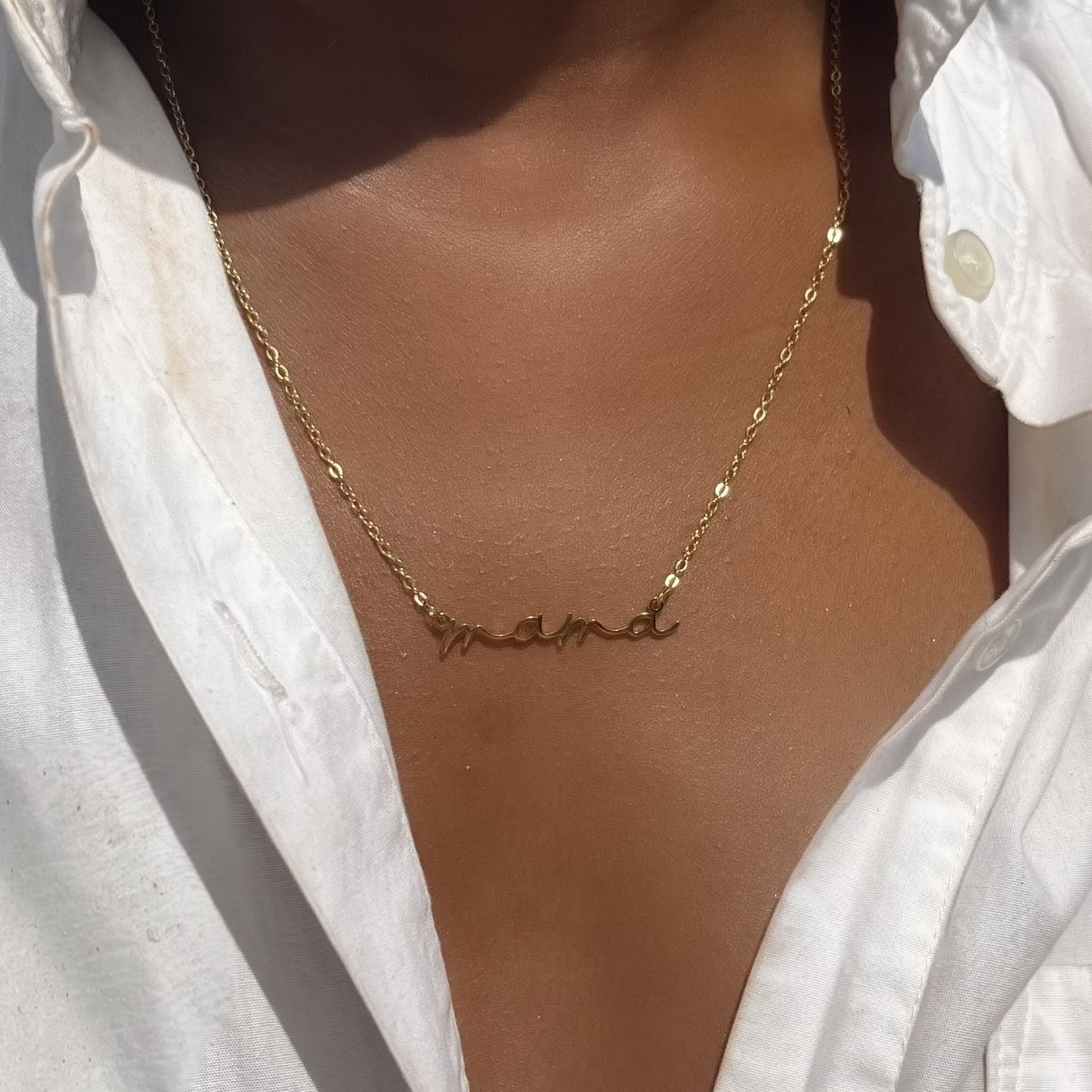 Gold necklace with a name pendant worn by a person in a white shirt.