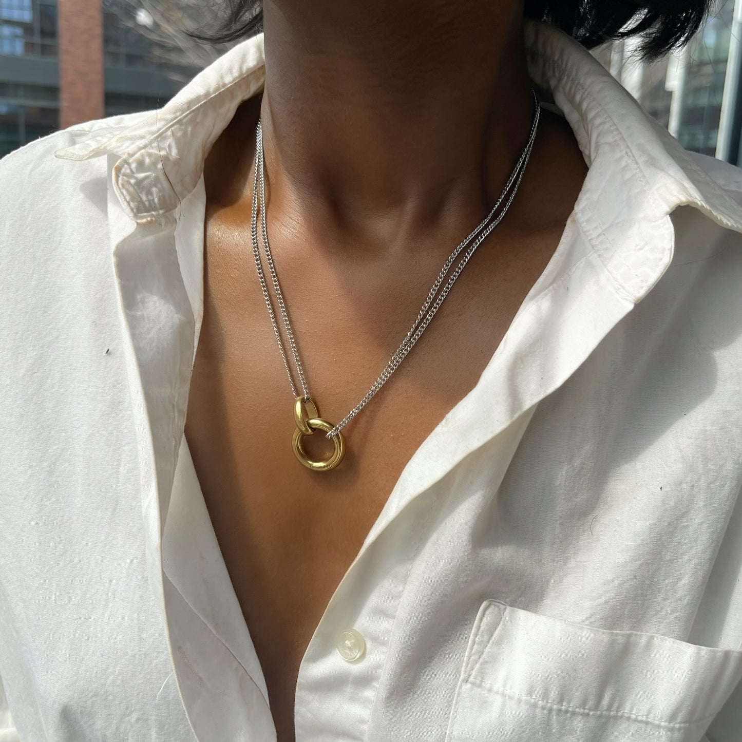 Necklace with a gold clasp worn by a person in a white shirt.