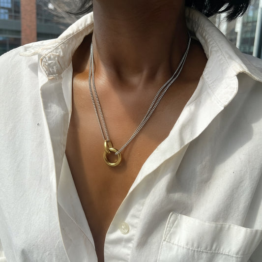 Necklace with a gold clasp worn by a person in a white shirt.