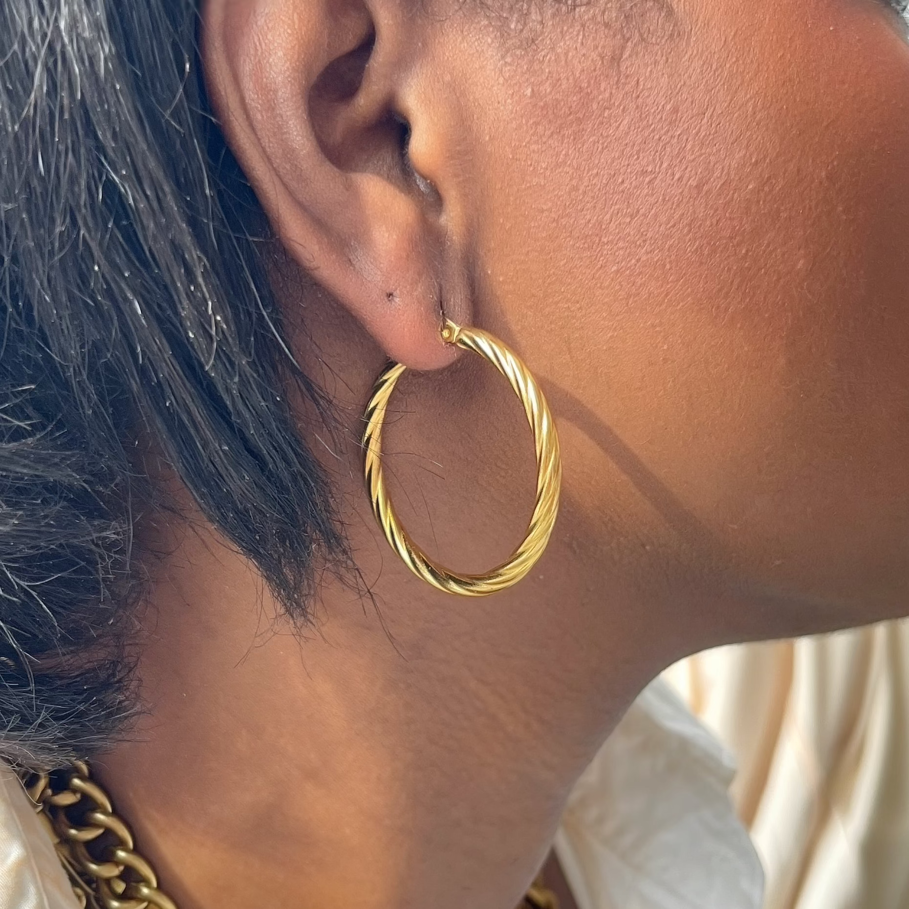 Close-up of a person wearing a gold hoop earring and necklace.