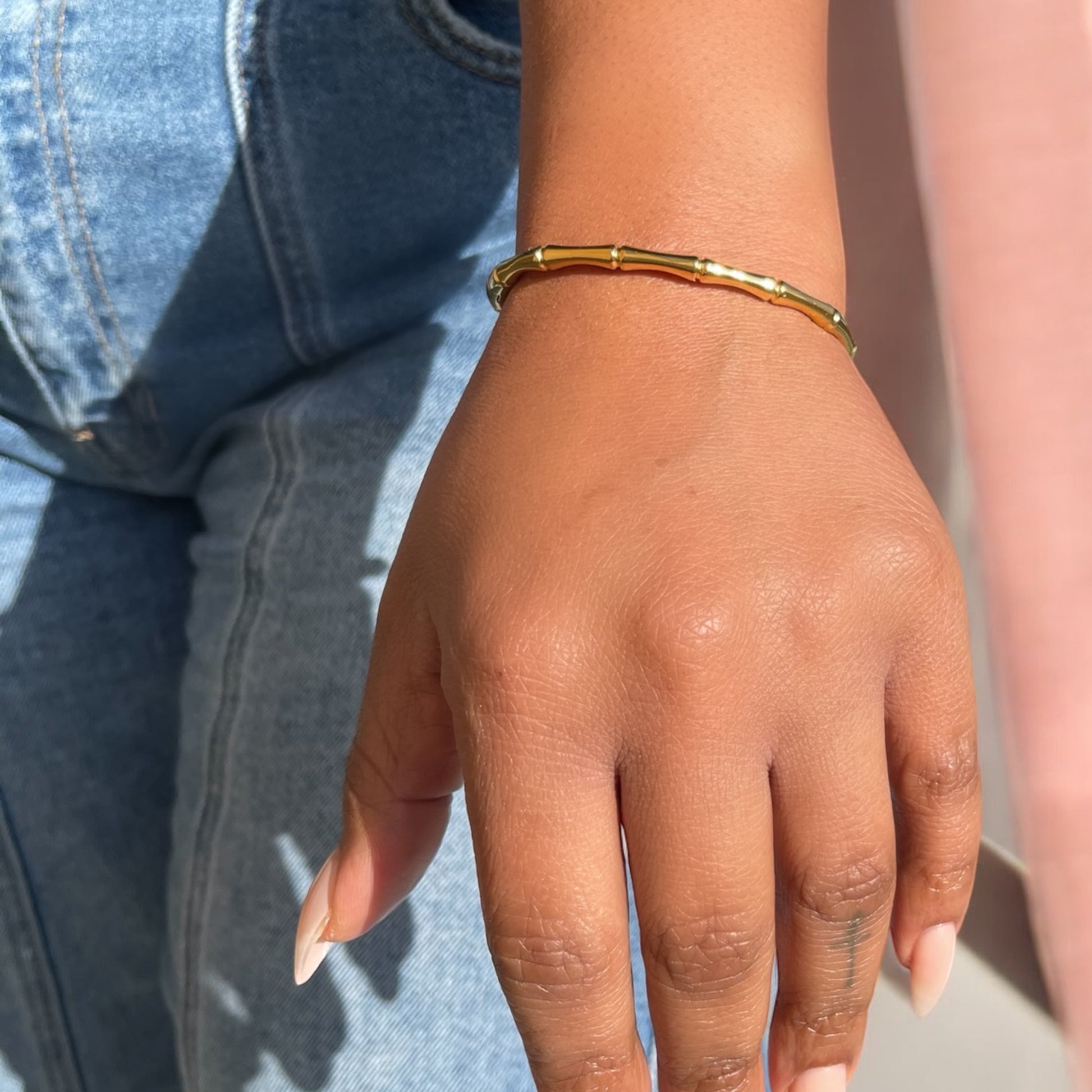 Hand wearing a gold bamboo bracelet with a blurred background