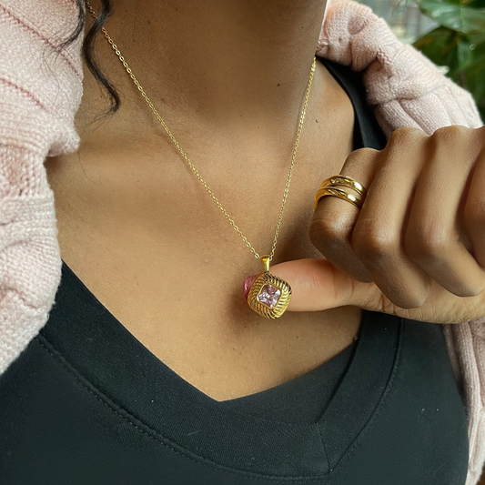 Person wearing a gold necklace with a pink pendant and multiple rings.