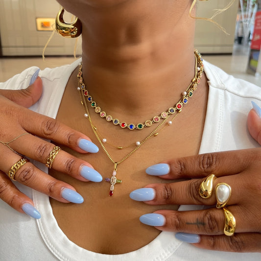 Close-up of a person wearing gold jewelry including necklaces, earrings, and rings with a white background.