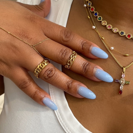 Close-up of a person wearing gold jewelry with a cross pendant, gold rings, and blue nail polish.