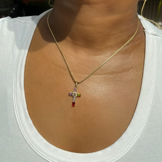 Gold necklace with a cross pendant worn by a person in a white shirt.