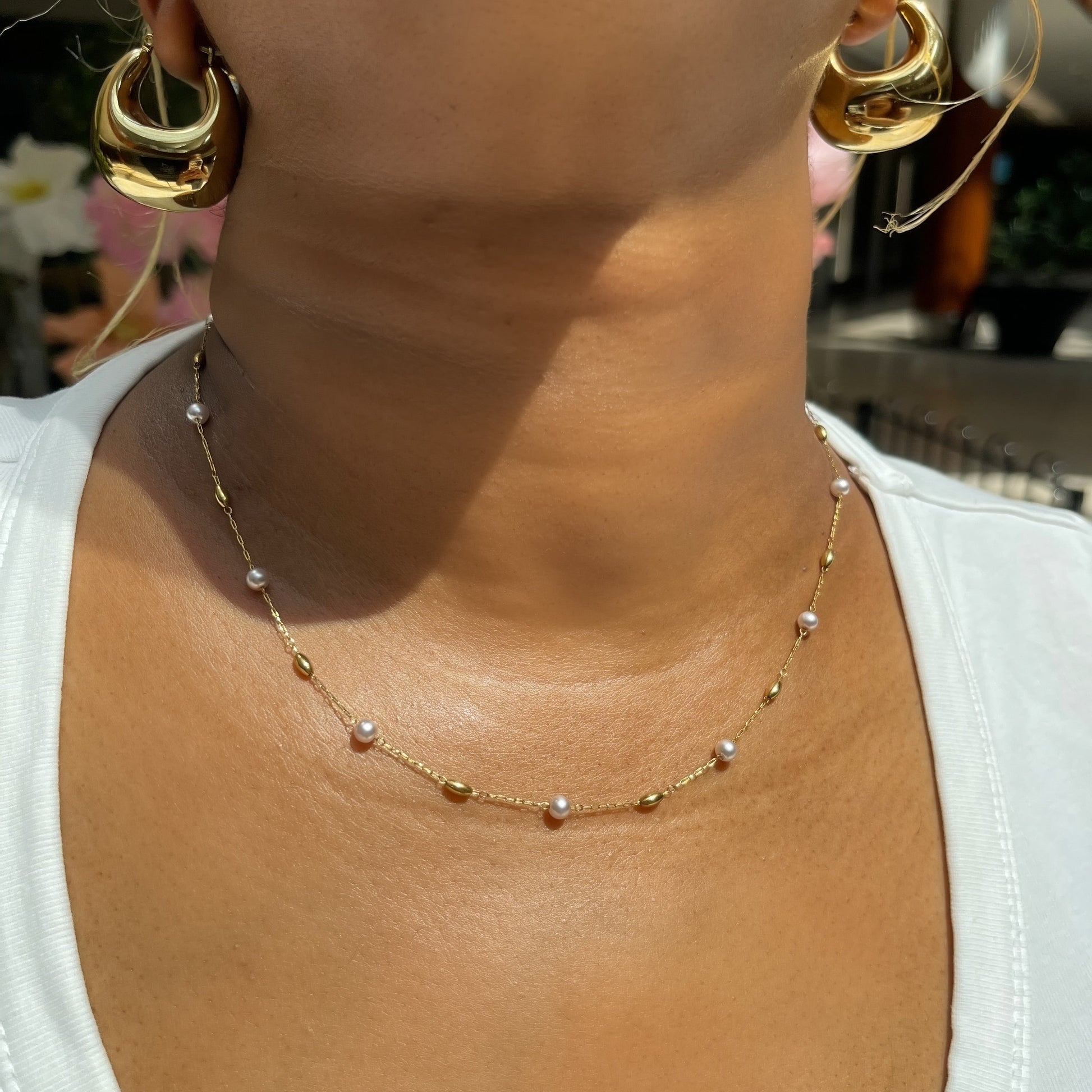 Gold necklace and earrings on a person wearing a white top.