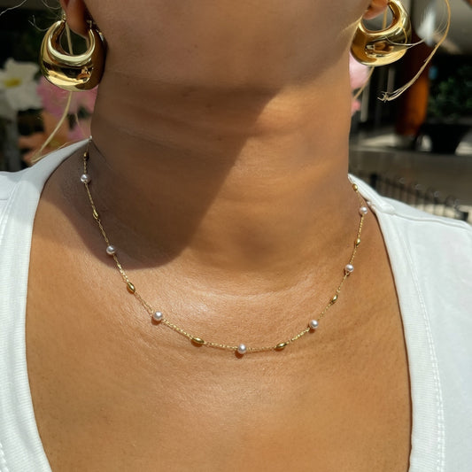 Gold necklace and earrings on a person wearing a white top.