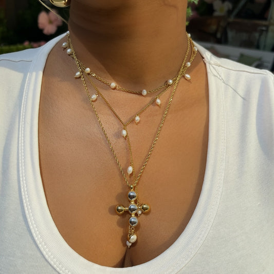 Person wearing a gold necklace with a cross pendant and pearl accents.